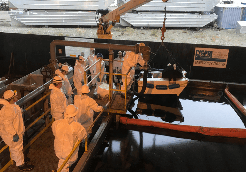 Workers in protective suits by docked boat